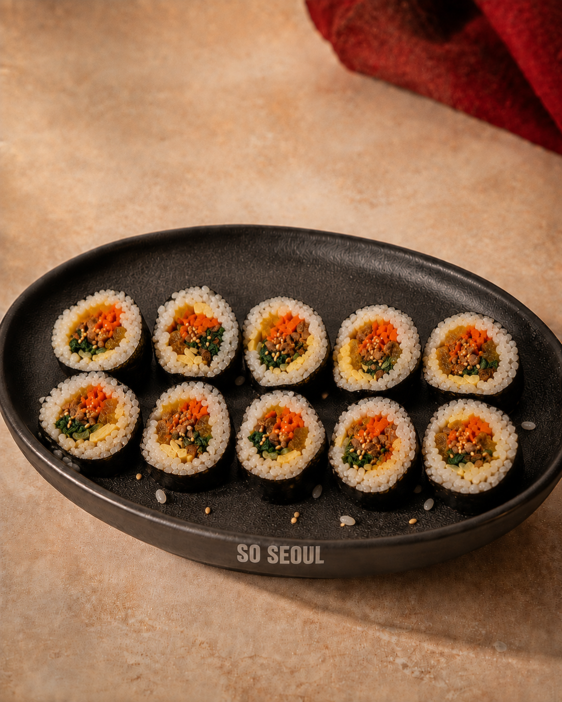 Ten hand-cut So Seoul kimbap pieces with naturally uneven rice and a few loose grains on the plate.